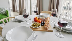 Een eettafel gedekt met borden, glazen en een houten plank met olijven, druiven, een appel en een stokbrood.