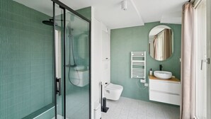 Een moderne badkamer met een glazen douchecabine, toilet, wastafel met spiegel en een handdoekrek.