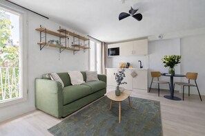 A modern living space with a green sofa, a small round table with a vase, a kitchen area with a microwave, and a dining table with chairs. - Lavie Maison : Spacious Studio near Montmartre (Paris)