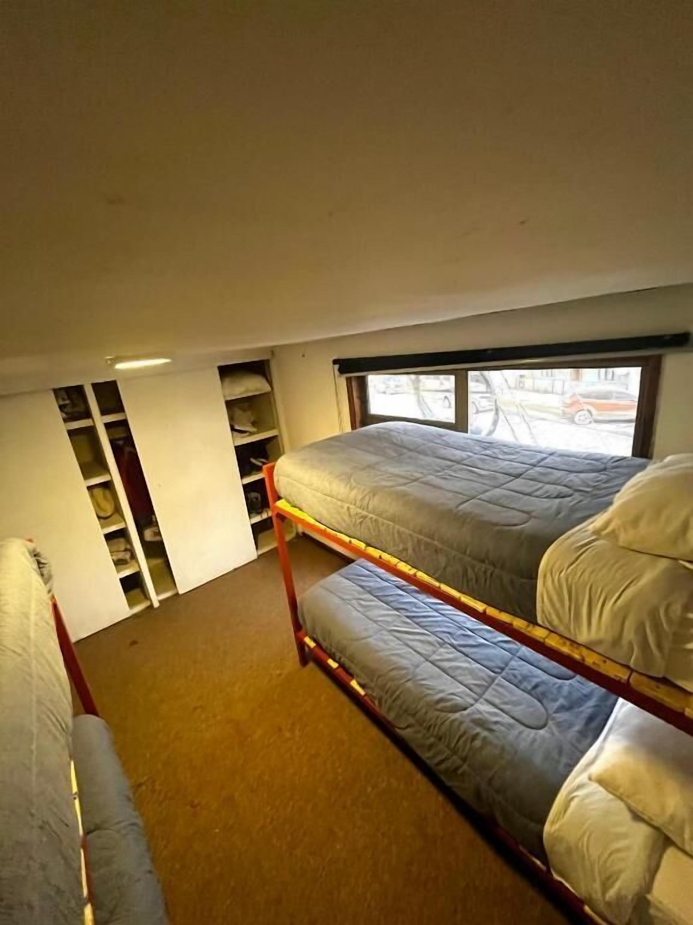 Ein Schlafsaalzimmer mit Etagenbetten, einem Fenster mit Blick auf die Straße und eingebauten Regalen.