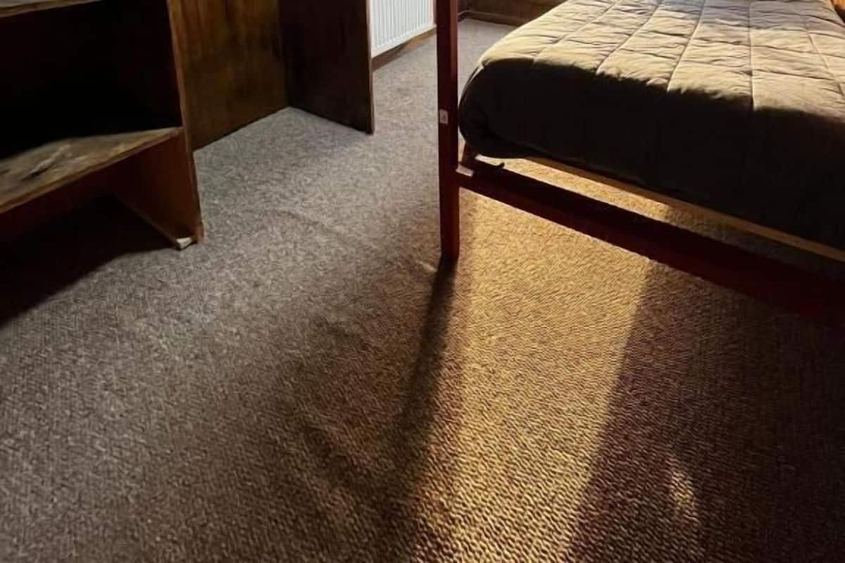 Una cama litera con ventana, un armario de madera y un radiador.