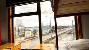A room with a bunk bed, a wooden desk, and a large window offering a view of a street and buildings.