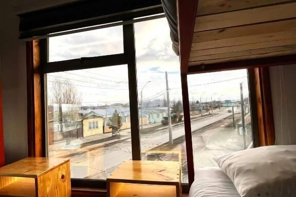Una habitación con una cama litera, un escritorio de madera y un ventanal que ofrece vistas a la calle y edificios.