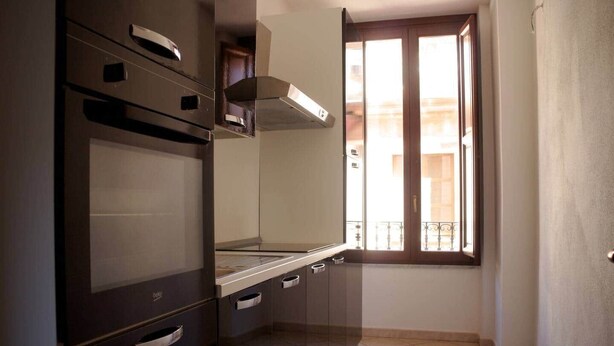 A kitchen with a stove, oven, and a window with a balcony view. - Sa Costa 18 (Bosa)