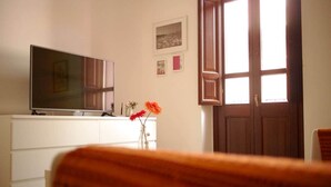 A living room with a TV on a white cabinet, a wooden chair in the foreground, and a door with a window. - Sa Costa 18 (Bosa)
