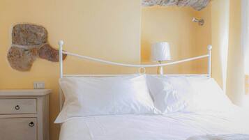 Una cama con sábanas blancas y estructura metálica, una mesita de noche con lámpara y una decoración de roca montada en la pared.