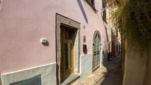 A narrow alleyway with a building featuring a wooden door and a small set of steps leading to the entrance. - Sardinian Gallery S'Intrada (Bosa)