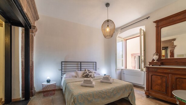 A bedroom with a bed, bedside table, and a hanging light fixture. - Sardinian Gallery S'Intrada (Bosa)