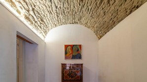 An interior hallway with a textured ceiling, a painting on the wall, and a wooden cabinet. - Sardinian Gallery S'Intrada (Bosa)