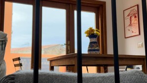 Una habitació amb un gran finestral, una taula de fusta amb un ram de flors i un quadre al mur.