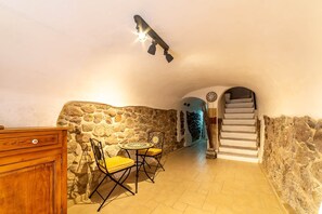 A stone-walled interior with a dining area, a staircase, and a ceiling light fixture. - Sardinian Gallery Seminario (Bosa)