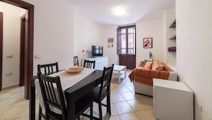 Un ambiente compatto con angolo pranzo, divano, televisore e un piccolo frigorifero.
