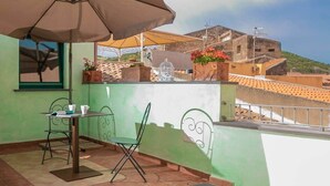 Een balkon met een tafel en stoelen, een grote parasol, potplanten en een uitzicht op gebouwen op de achtergrond.