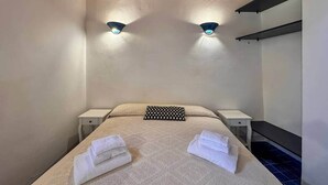 Un dormitorio con una cama, dos mesitas de noche, un almohadón a cuadros y dos luces fijadas a la pared.