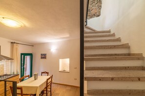 Un comedor con mesa y sillas, una cocina con estufa, y una escalera de piedra.