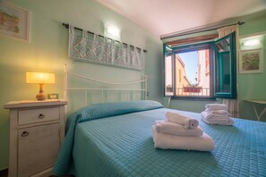 Un dormitorio con cama, mesita de noche con lámpara, ventana con vistas y un adorno en la pared.