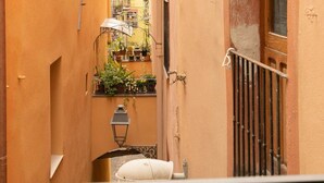 Un vicolo stretto con un oggetto cilindrico bianco, un lampione in metallo e piante in vaso su un balcone.