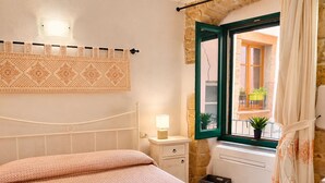 Una camera da letto con un letto, un comodino, una lampada, una finestra vista e un arazzo decorato appeso al muro.