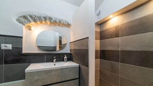 Un baño con un lavamanos blanco, un espejo redondo y paredes de azulejos oscuros.
