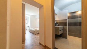 Un pasillo que lleva a un dormitorio con cama y un baño con lavamanos moderno y paredes con azulejos.