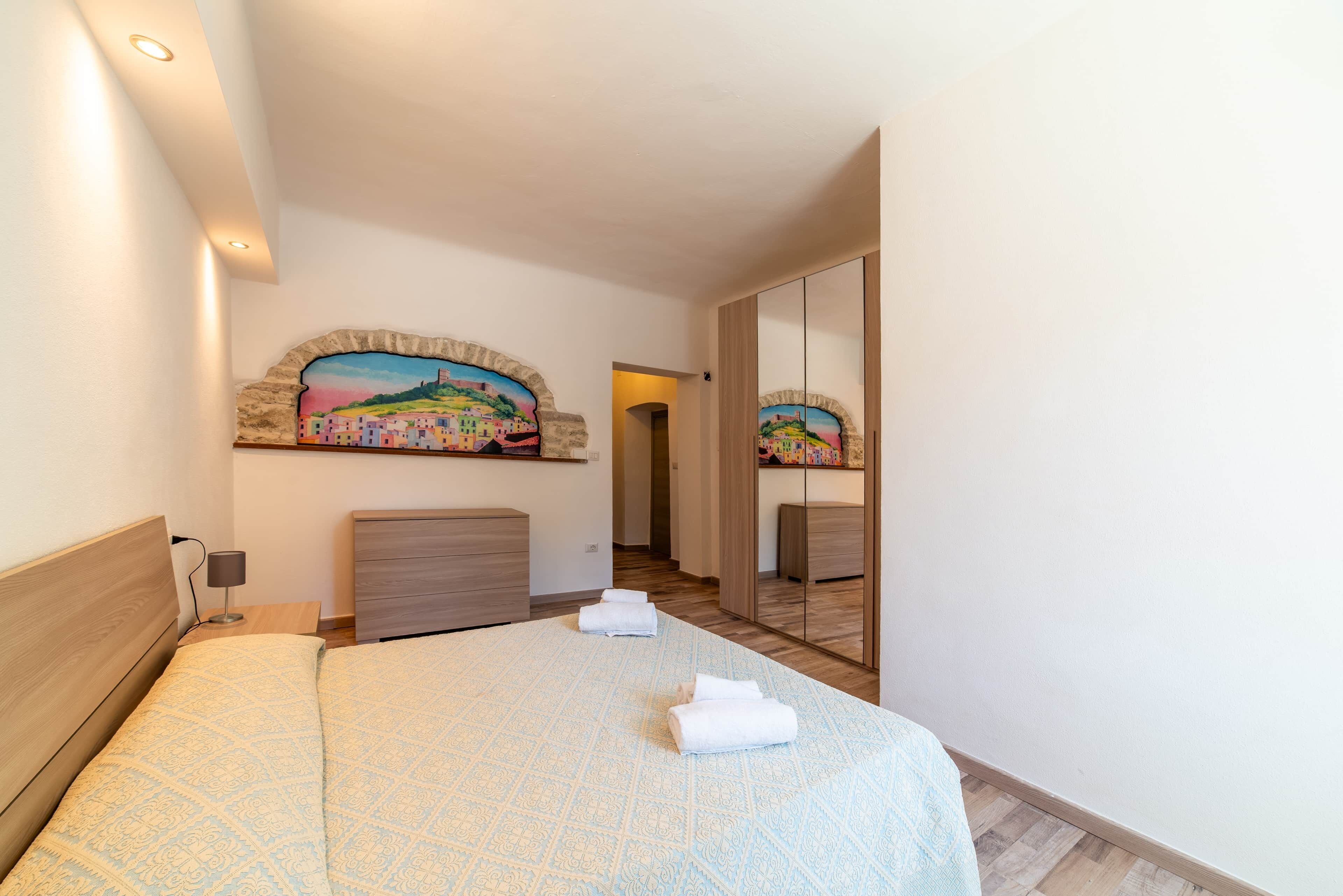 Een hotelkamer met een bed, nachtkastje, dressoir, schilderij en spiegel.