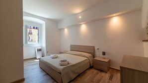 Un dormitorio con cama, mesitas de noche, ventana y puerta.