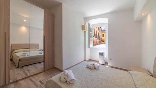 Un dormitorio con cama, espejo, ventana y vistas a edificios.