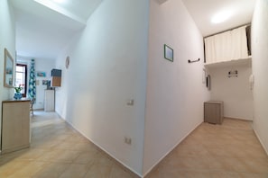 A hallway with a tiled floor, a door, and a small cabinet. - Sa Piatta 27 (Bosa)