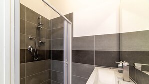 Ein modernes Badezimmer mit Duschkabine aus Glas, einem weißen Waschbecken und dunkel gefliesten Wänden.