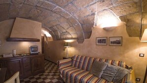 A cozy room with a checkered floor, a striped sofa, a small kitchen area with a microwave, and a stone ceiling. - Sardinian Gallery Vittorio (Bosa)