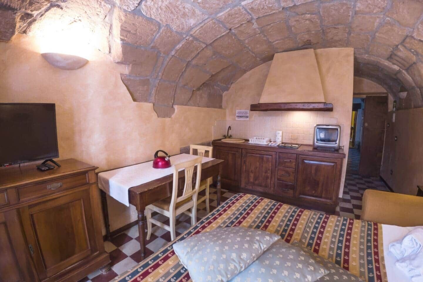 Habitació acollidora amb sostre d'arc de pedra, escriptori de fusta, televisió, petita cuina i una alfàbbra amb disseny.