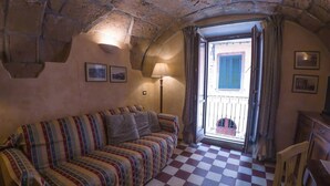 A cozy room with a checkered floor, a striped sofa, a lamp, and a balcony with blue shutters. - Sardinian Gallery Vittorio (Bosa)