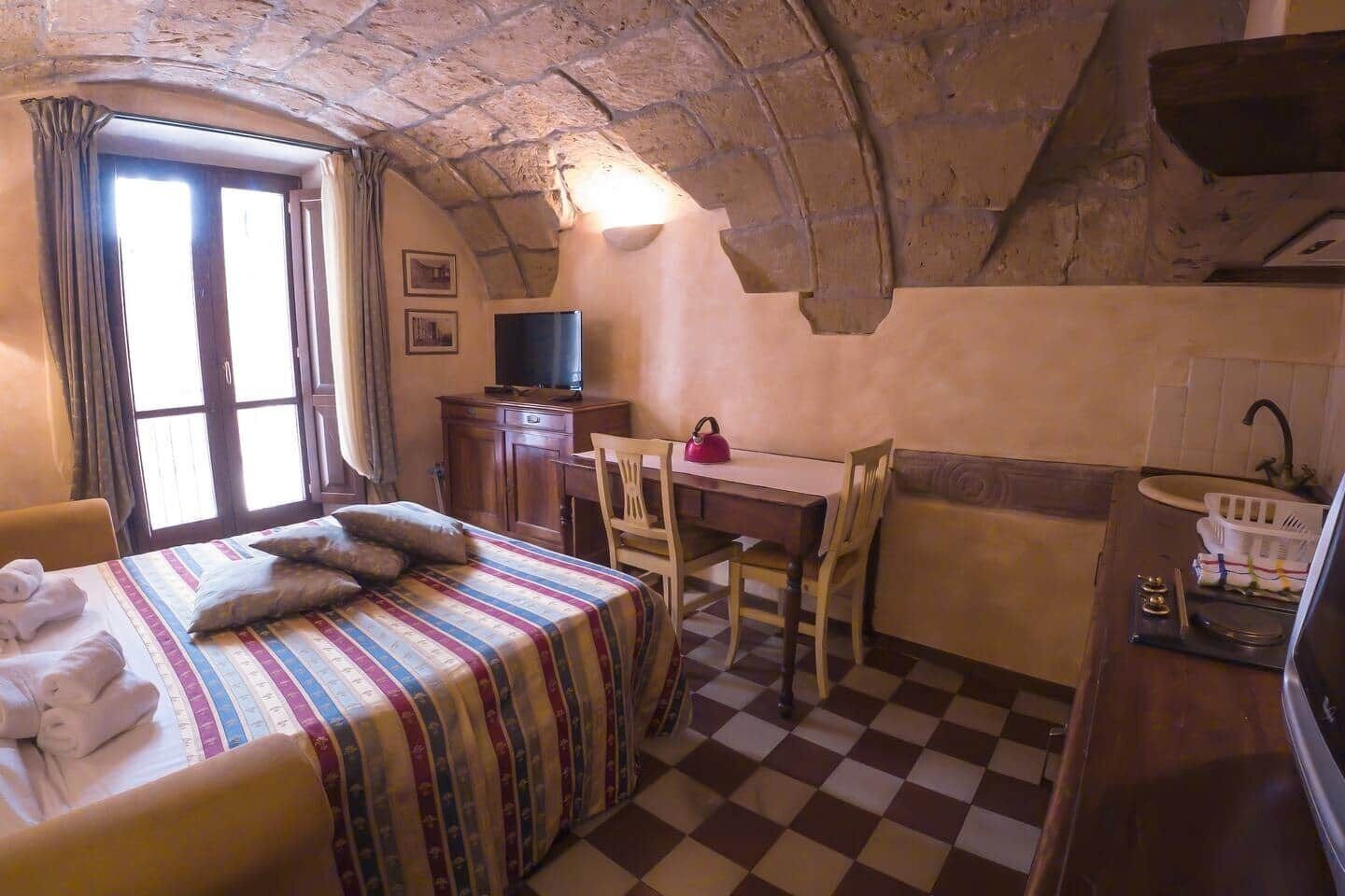 Una habitación acogedora con cama, escritorio, silla, televisor y lavamanos.