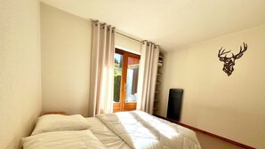 A bedroom with a bed, a window with curtains, a wall-mounted deer head decoration, and a small black object on the wall. - Bright apartment in Combloux, near ski (Combloux)