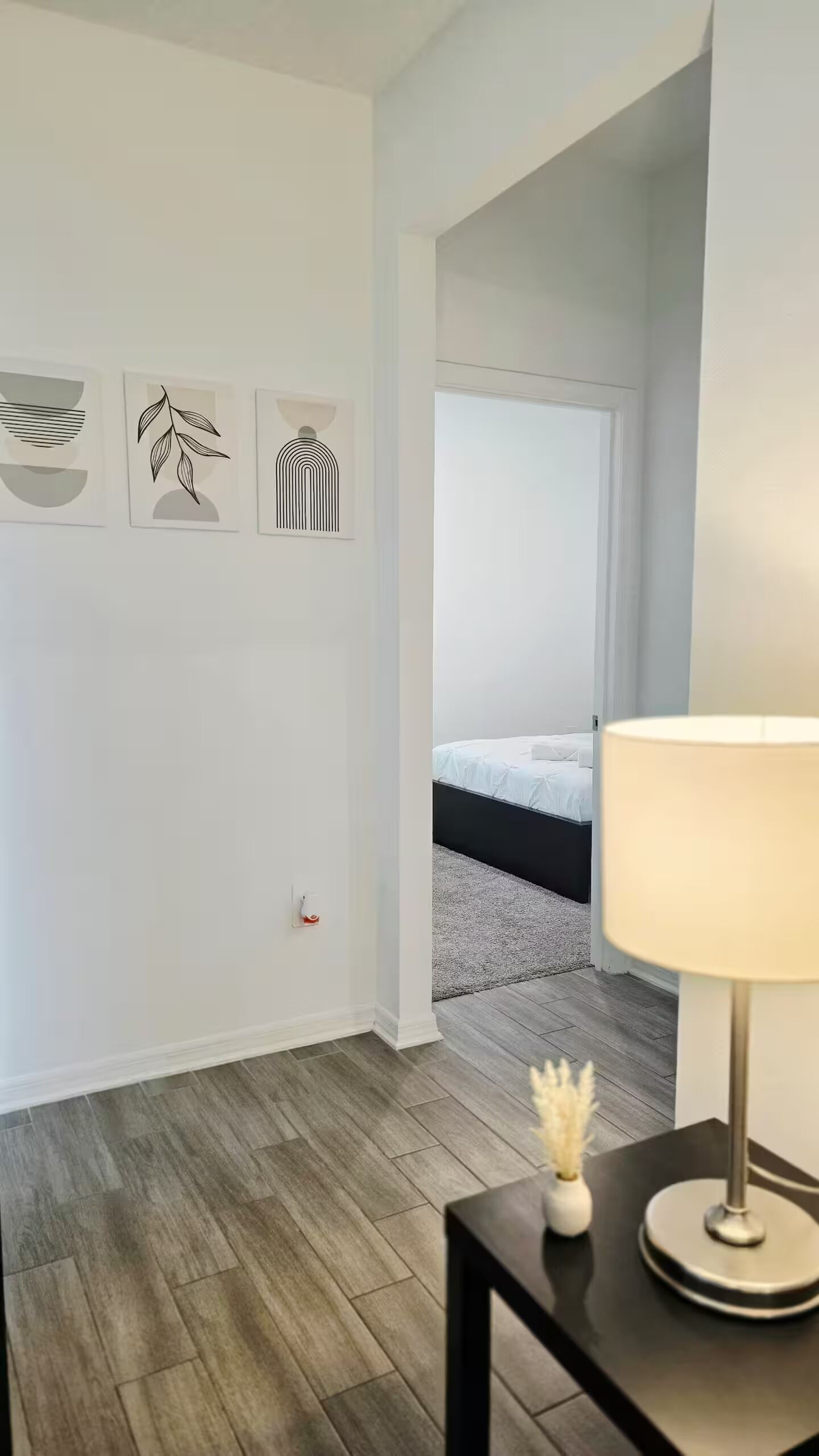 Um quarto moderno com uma cama, uma mesa de cabeceira com abajur e três quadros na parede.
