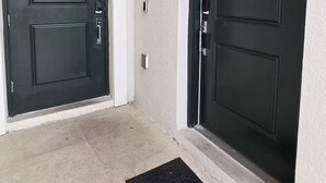 Zwei dunkle Türen mit einer strukturierten Wand und einer schwarzen Fußmatte davor.