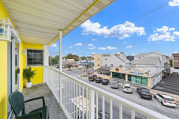 A balcony with a view of a street, a building with a sign for 'Devey's Brewing Beach', and parked cars. - 70 Steps to the Sand • 2BR/1BA • 2 Balconies • Sleeps 6 (Dewey Beach)