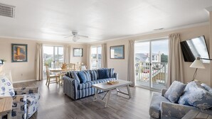 A spacious living room with a blue-striped sofa, a wooden coffee table, and a balcony with a view of the city. - 70 Steps to the Sand • 2BR/1BA • 2 Balconies • Sleeps 6 (Dewey Beach)