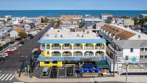 A multi-story building with a blue and yellow facade, a beach view, and a parking area with customer parking signs. - 70 Steps to the Sand • 2BR/1BA • 2 Balconies • Sleeps 6 (Dewey Beach)