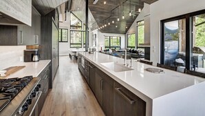 A modern kitchen with a large island, dark wood cabinets, and a stainless steel stove. - Walk-to-Ski Retreat | Serac Lodge (Breckenridge)