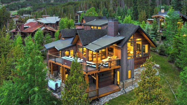 A large, multi-story wooden cabin with a balcony and hot tub, surrounded by dense forest and mountains. - Walk-to-Ski Retreat | Serac Lodge (Breckenridge)