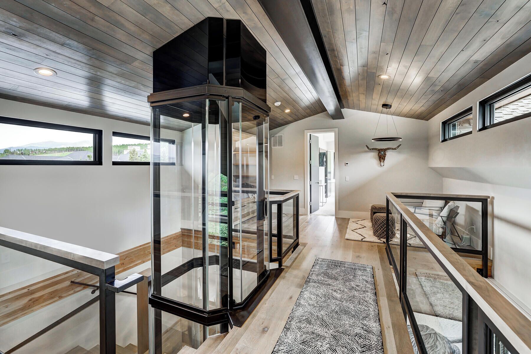 A modern interior with a glass staircase, wooden floors, and a view of the outdoors.
