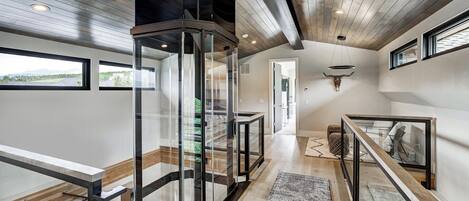 A modern interior with a glass staircase, wooden floors, and a view of the outdoors.