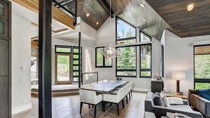 A spacious living area with a large dining table, comfortable seating, and large windows offering views of the outdoors. - Walk-to-Ski Retreat | Serac Lodge (Breckenridge)