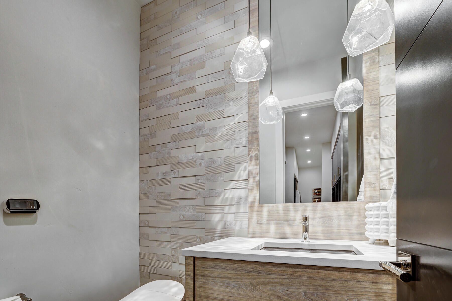 A modern bathroom with a wooden wall panel, a white sink, and a mirror with a hexagonal light fixture.
