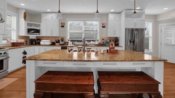 A kitchen with white cabinets, a granite countertop, a stainless steel refrigerator, and a double sink.