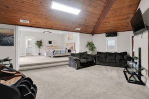 A spacious living area with a high ceiling, a sofa, a television, and a staircase leading to another room. - 6 Bedrooms | Bar Lounge & Pool | Foosball (Wetumpka)