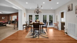 A dining area with a wooden table and chairs, a chandelier, and a view through glass doors.