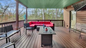 A covered deck with a red sofa, two chairs, a table, and a ceiling fan.