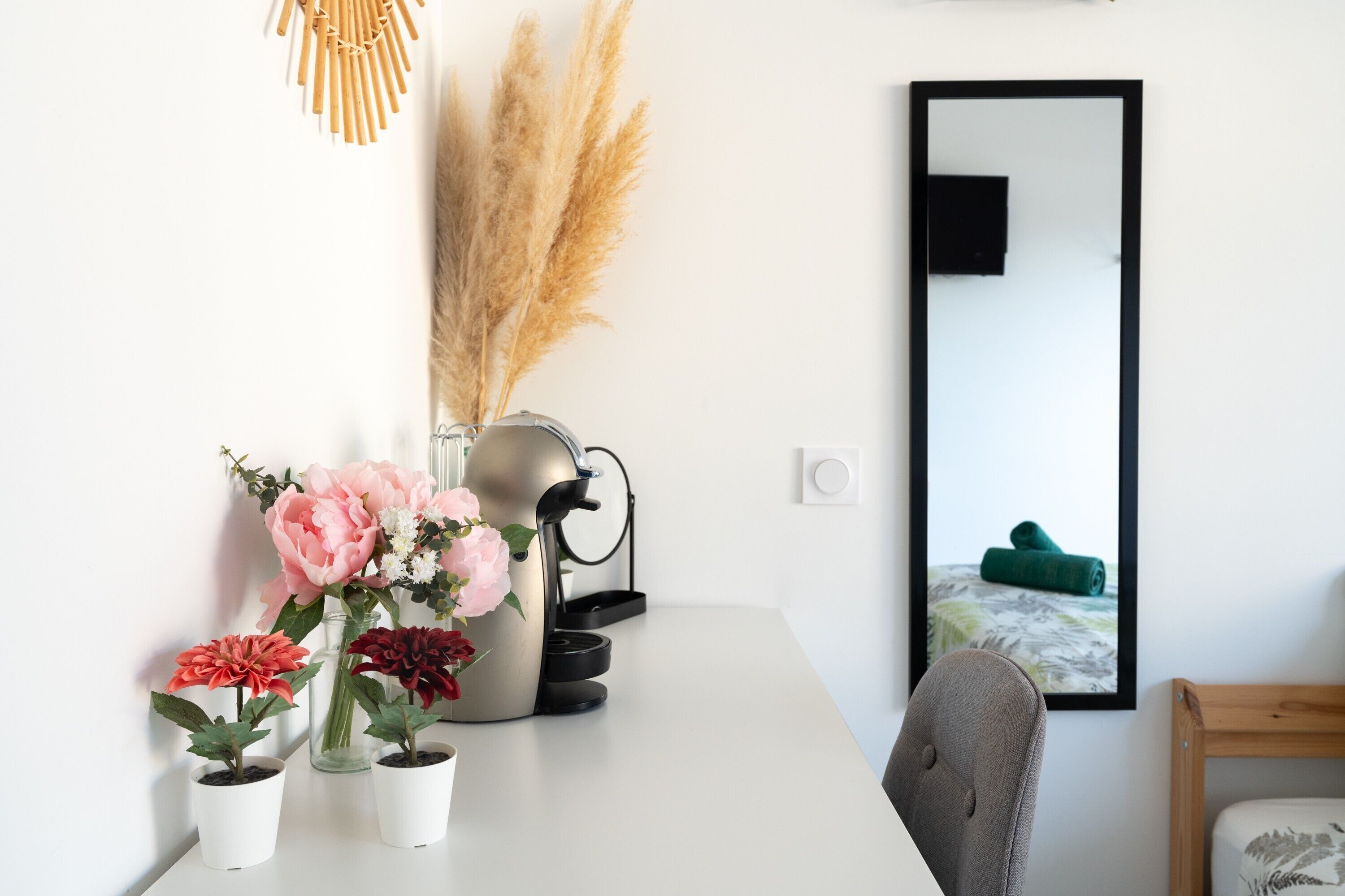 A white table with potted plants, a coffee maker, and a mirror.